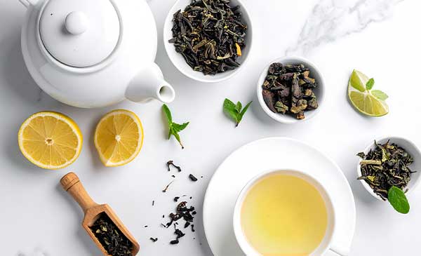 white teapot and cup with green tea and citrus slices