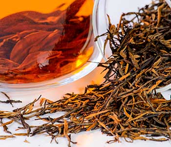 close up picture of golden monkey tea with cup of tea showing the amber color